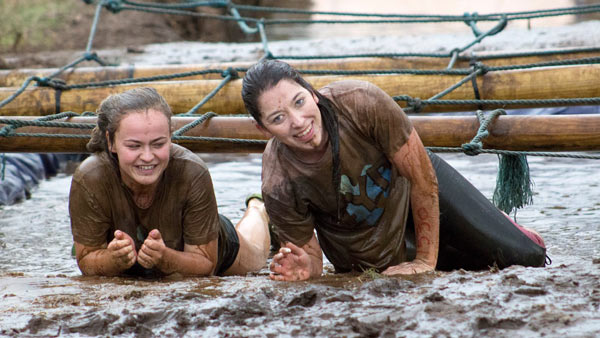 Two women army crawling through mud on an Eight Point Two obstacle course race